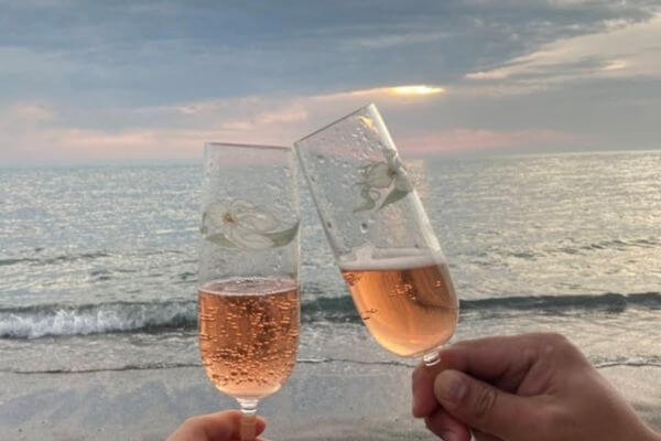 Two glasses of champagne being held by people on the beach