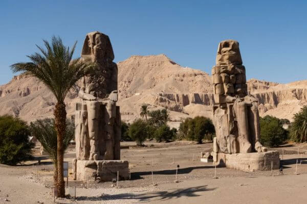 The two large stone statues of the Colossi of Memnon standing in the open desert in Luxor, Egypt.