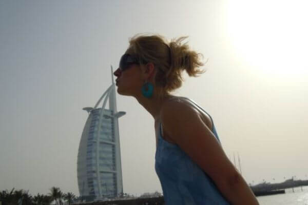 Kissing Burj Al Arab, Dubai A woman poses playfully as if kissing the Burj Al Arab in Dubai, with the iconic sail-shaped hotel in the background. The sun is shining behind her, creating a soft glow in the sky.
