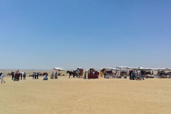 Horse Carriages around Giza Pyramids, Egypt Horse carriages and souvenir stalls on the sandy ground around the Giza Pyramids in Egypt, with people walking around under a clear blue sky.