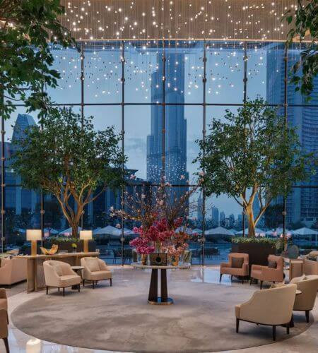 Lobby at Address Sky View A bright hotel lobby at Address Sky View in Dubai with cozy seating, tall trees, and floor-to-ceiling windows showing the Burj Khalifa skyline, offering a relaxing space for guests looking for hotels near Dubai Mall and Burj Khalifa.