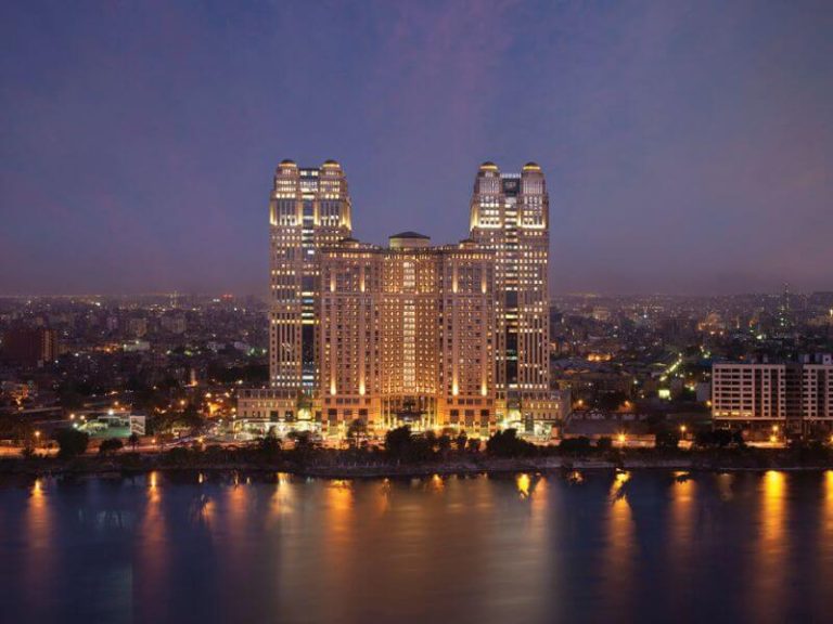Fairmont Nile City hotel lit up at night, with its twin towers reflected in the Nile River.