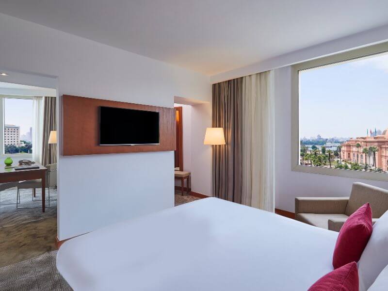 A Capital Suite room at Steigenberger Hotel in Cairo, with a large bed, TV and a window view of the Egyptian Museum.
