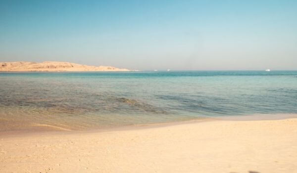 Mahmya Island, Egypt A quiet stretch of Mahmya Island in Egypt with soft sand leading to clear blue water. Gentle waves touch the shore under a bright, sunny sky.