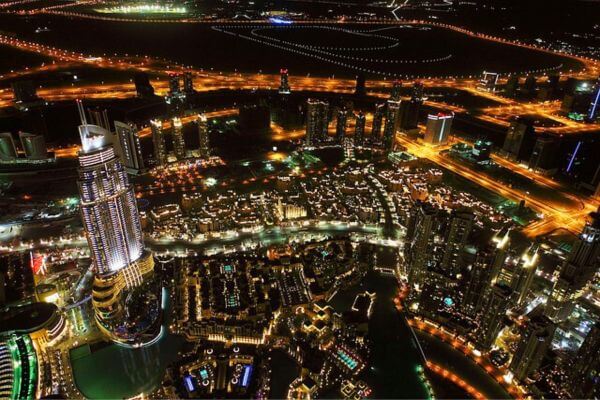 Night view from the top of Burj Khalifa, Dubai A nighttime view from the Burj Khalifa shows Dubai glowing with golden streetlights and illuminated skyscrapers. The city’s roads form bright patterns, and the tall buildings reflect lights over the water below. The scene captures the lively energy of Dubai after dark.