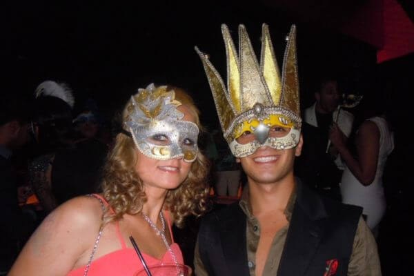 Venice night in Dubai's nightclub Two people wearing decorative Venetian masks pose together at Armani Privé nightclub in Dubai during Venice Night. The crowd behind them enjoys the party atmosphere with colorful lights and music.