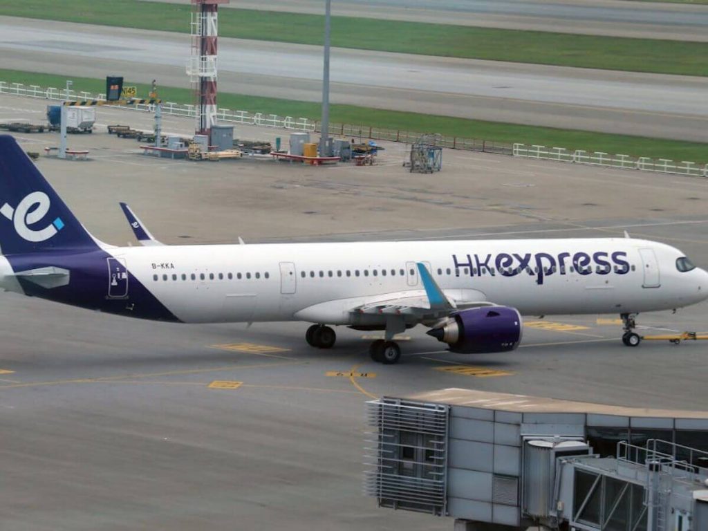 HK Express Plane A white HK Express airplane is taxiing on an airport runway. The aircraft features purple lettering and tail accents, conveying a modern, efficient tone.