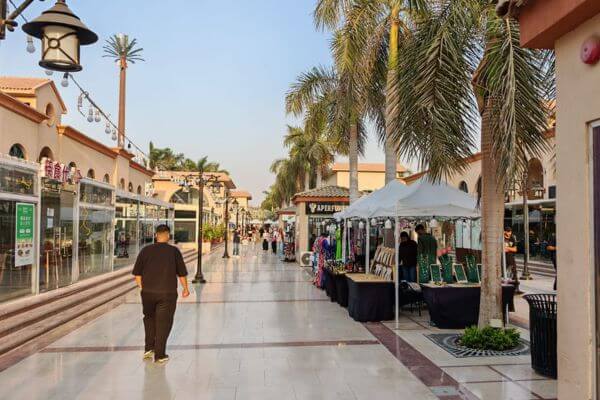 An open air shopping street in New Cairo, Egypt, with small shops, palm trees and outdoor market stalls.