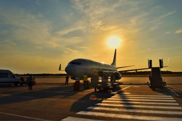 Airplane A commercial airplane is parked on the tarmac at sunset, casting long shadows across the ground. Airport staff and equipment surround the aircraft as it prepares for boarding or maintenance.