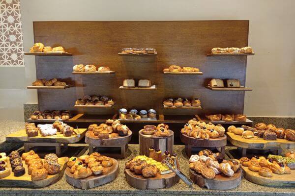 Jaz Tamrina, pastries in the restaurant A large pastry display at the Jaz Tamerina Hotel in Almaza Bay, Marsa Matrouh. The setup includes rows of fresh croissants, rolls, muffins, and other baked treats arranged neatly on wooden stands and trays.