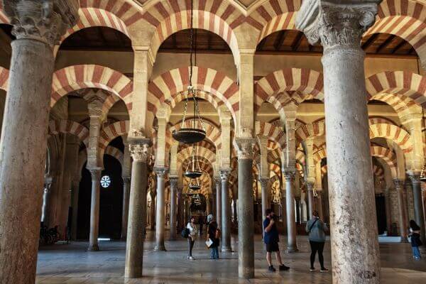 Mezquita, Cordoba Interior of the Mezquita in Cordoba with rows of stone columns and red and white striped arches, with visitors walking through the historic prayer hall
