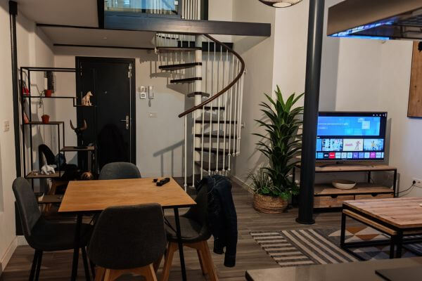 RentalSevilla Alameda, Seville Modern rental apartment interior of RentalSevilla Alameda in Seville with wooden dining table, spiral staircase leading to upper level, living area with TV, and green plants