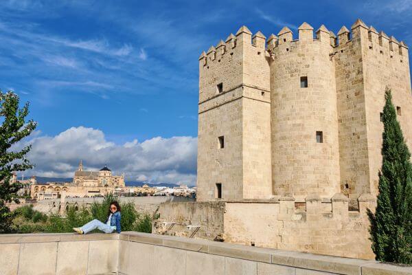 Roman Bridge, Cordoba A girl sitting by the stone Calahorra Tower next to the Roman Bridge in Cordoba, Spain with the Mezquita Cathedral visible in the background under a blue sunny sky with white clouds