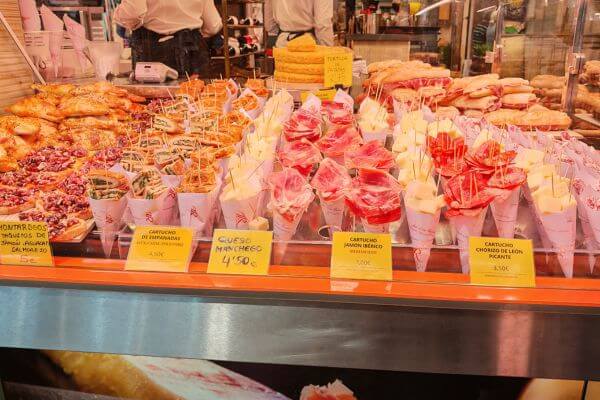 Colorful display of tapas and desserts at Mercado de Triana in Seville with pink and white treats in cups, pastries, and yellow price tags on the counter"
This captures the delicious variety of Spanish treats at this vibrant market!