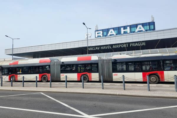 A public PID bus stopped outside Václav Havel Airport Prague, ready to take passengers to the city centre, with the Praha sign clearly visible on the airport building.