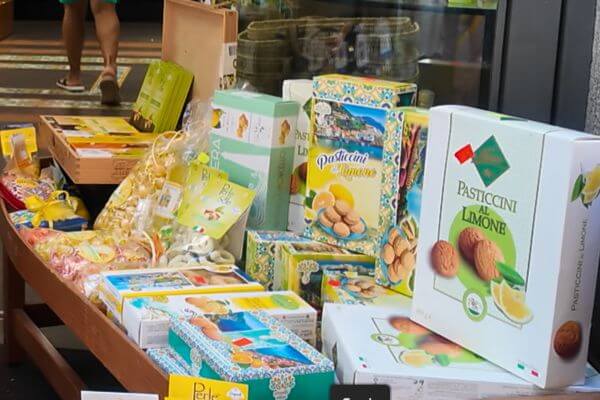 A shop display on the Amalfi Coast filled with lemon biscuits and sweets, including boxes of Pasticcini al Limone and other lemon treats packaged in colorful boxes.