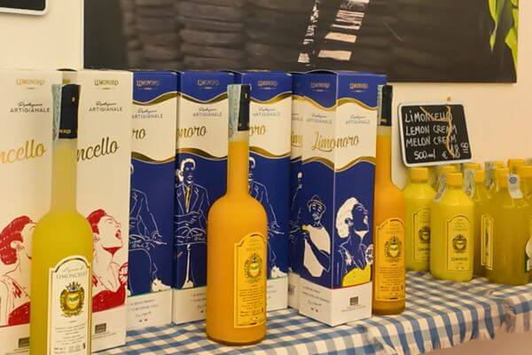 Bottles of Limoncello and lemon and melon cream by Limonoro on a shop shelf on the Amalfi Coast, displayed in blue and white boxes next to smaller bottles of lemon cream.