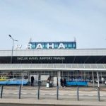 The front of Terminal 1 at Václav Havel Airport Prague, with the Praha sign on top of the building, taxis waiting outside, and passengers walking on the pavement.