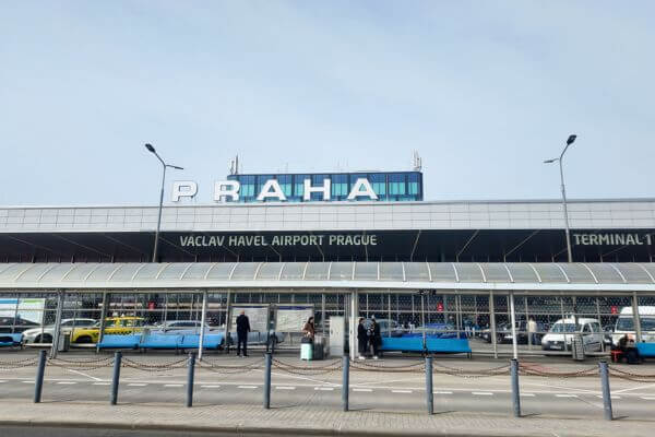 The front of Terminal 1 at Václav Havel Airport Prague, with the Praha sign on top of the building, taxis waiting outside, and passengers walking on the pavement.