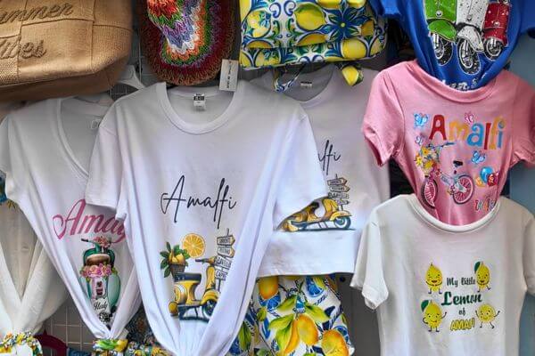Colorful Amalfi souvenir t-shirts for sale in a shop on the Amalfi Coast, featuring lemon and scooter prints.