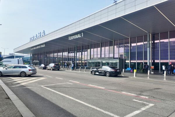 An Uber taxi waiting outside Terminal 1 at Václav Havel Airport Prague, with other cars dropping off and picking up passengers, and the Praha sign visible on the front of the building.