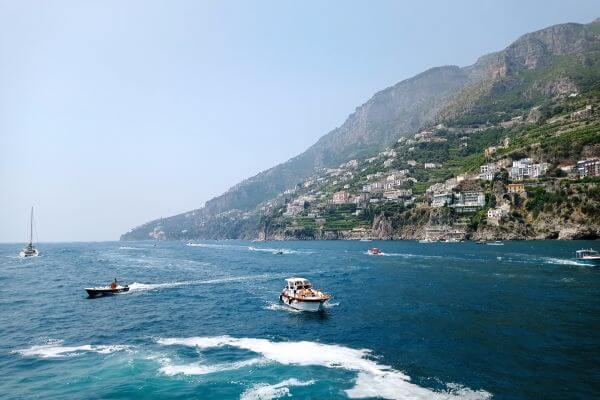 Amalfi Coast by public transport A view of the Amalfi Coast from the water, with boats on the sea and hillside villages visible along the cliffs.