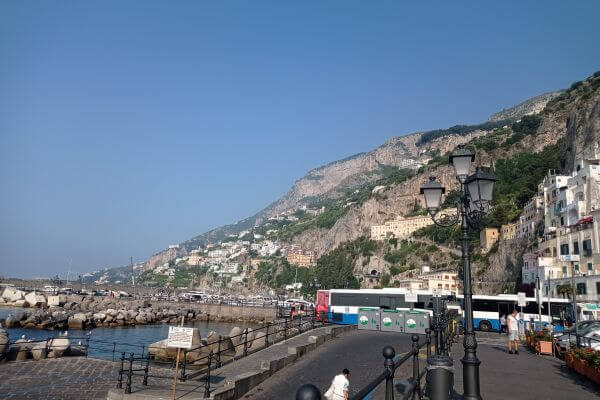 Amalfi Coast by taxi The waterfront street and bus stop in Amalfi town on the Amalfi Coast, Italy, with the hillside and sea in the background.