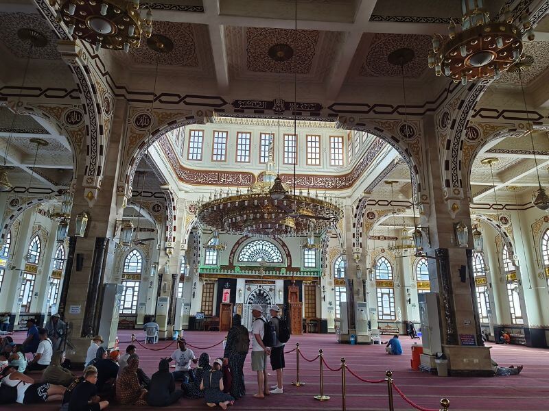 The interior of El Mina El Kabeer Mosque in Hurghada, Egypt, with decorated arches, a large chandelier and visitors inside.
